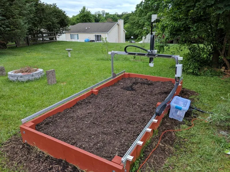 A freshly installed FarmBot over a raised bed of soil in an ordinary backyard